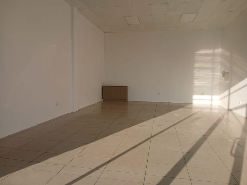 A vacant, open-plan retail space featuring neutral tiled flooring, a suspended ceiling with recessed lighting, and ample natural light.