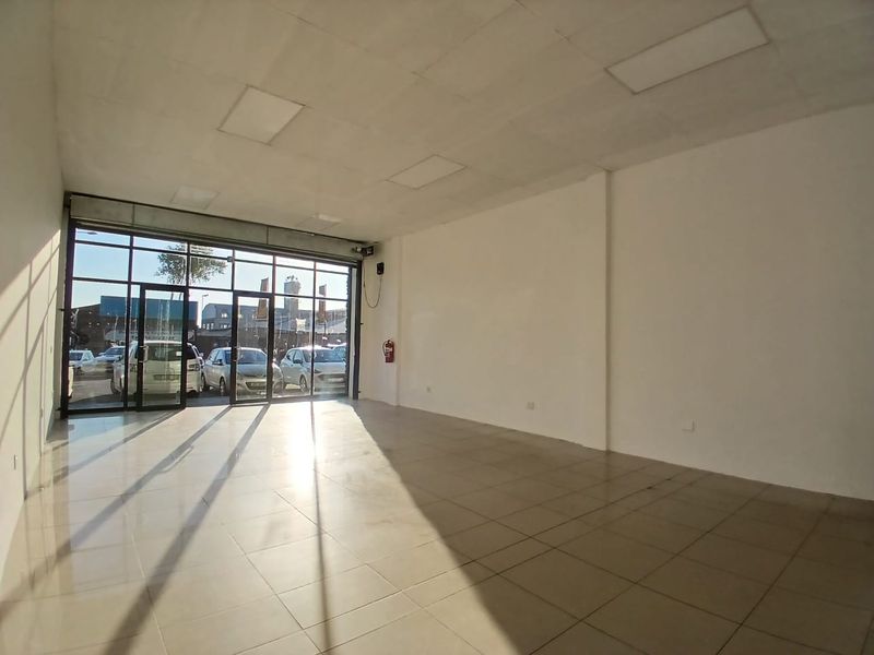 A bright, open-plan retail space featuring large glass storefront windows, tiled flooring, and a suspended ceiling with recessed lighting.