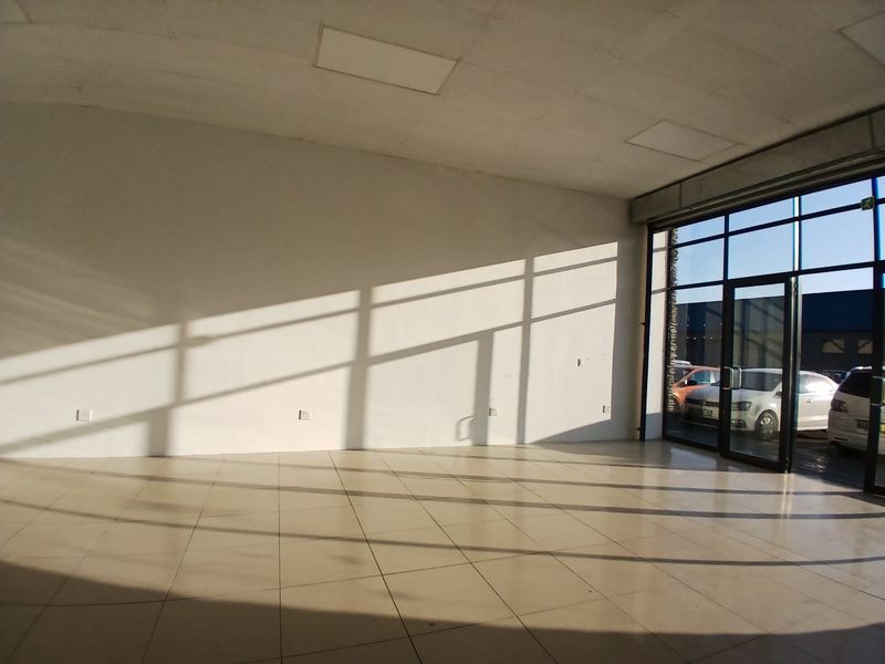 A bright, empty open-plan retail space featuring large glass storefront windows, tiled flooring, and recessed ceiling panels, ideal for a showroom or shop.