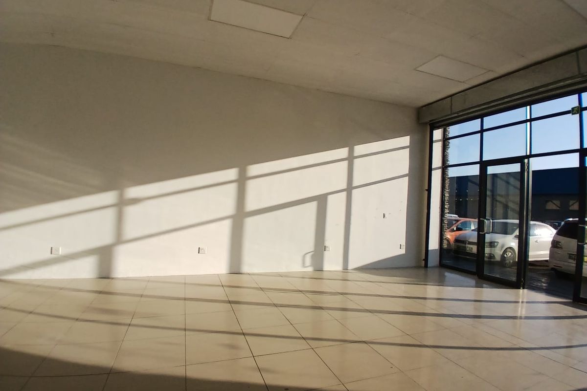 A bright, empty open-plan retail space featuring large glass storefront windows, tiled flooring, and recessed ceiling panels, ideal for a showroom or shop.