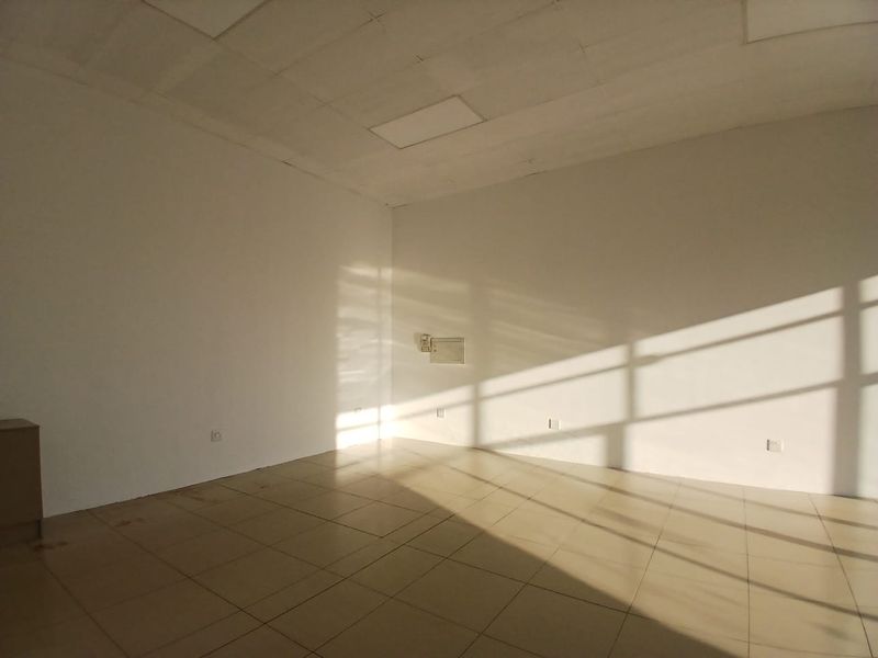 A vacant, open-plan retail space featuring tiled flooring, a suspended ceiling, and natural light streaming through large windows.