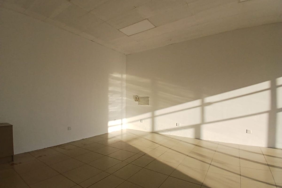 A vacant, open-plan retail space featuring tiled flooring, a suspended ceiling, and natural light streaming through large windows.