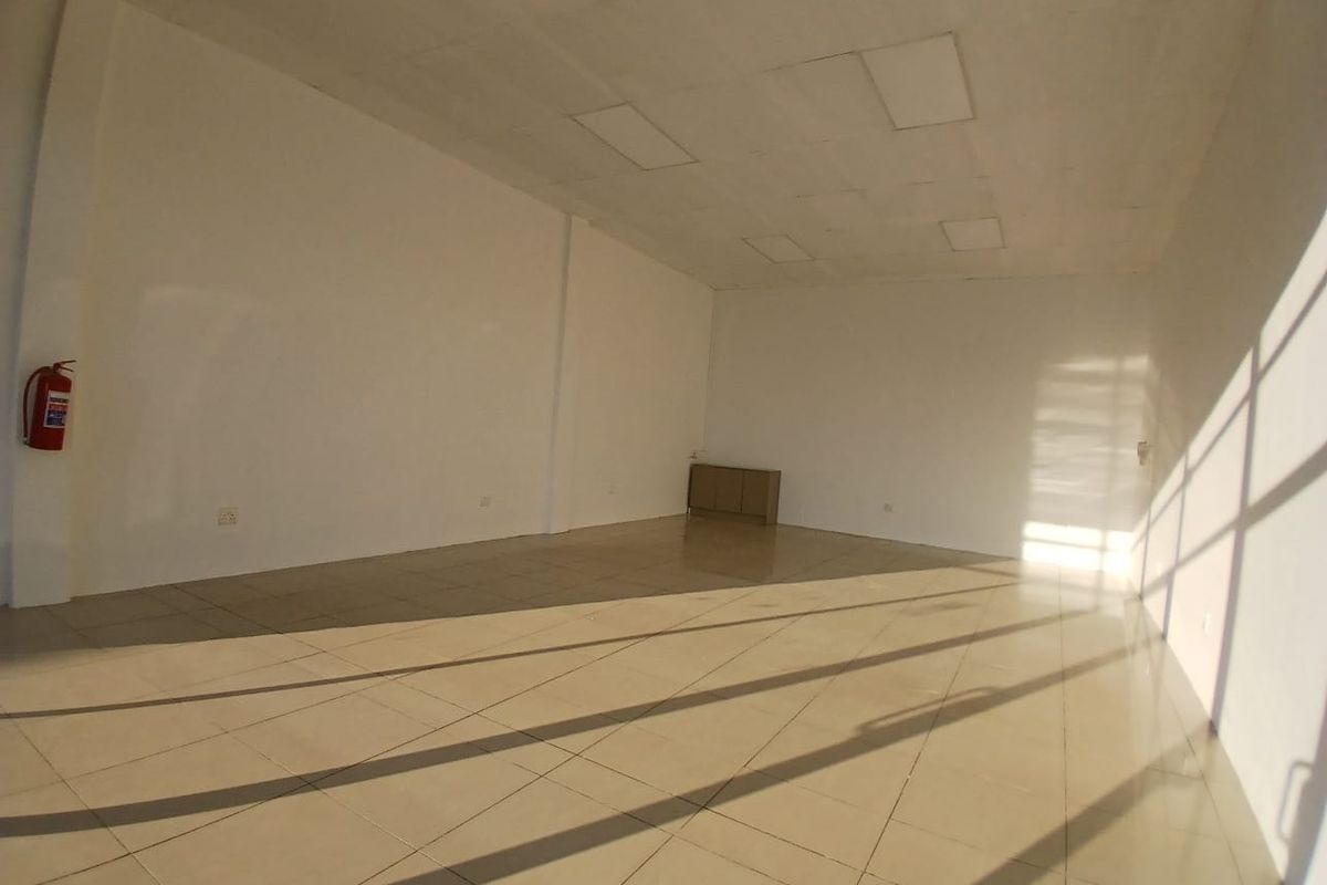A spacious, empty open-plan retail unit featuring tiled flooring, recessed ceiling lights, and a wall-mounted fire extinguisher.