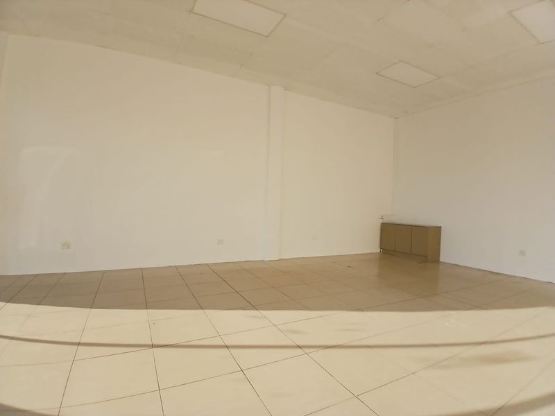 A vacant open-plan retail space featuring tiled flooring, recessed ceiling panels, and a small built-in storage cabinet.