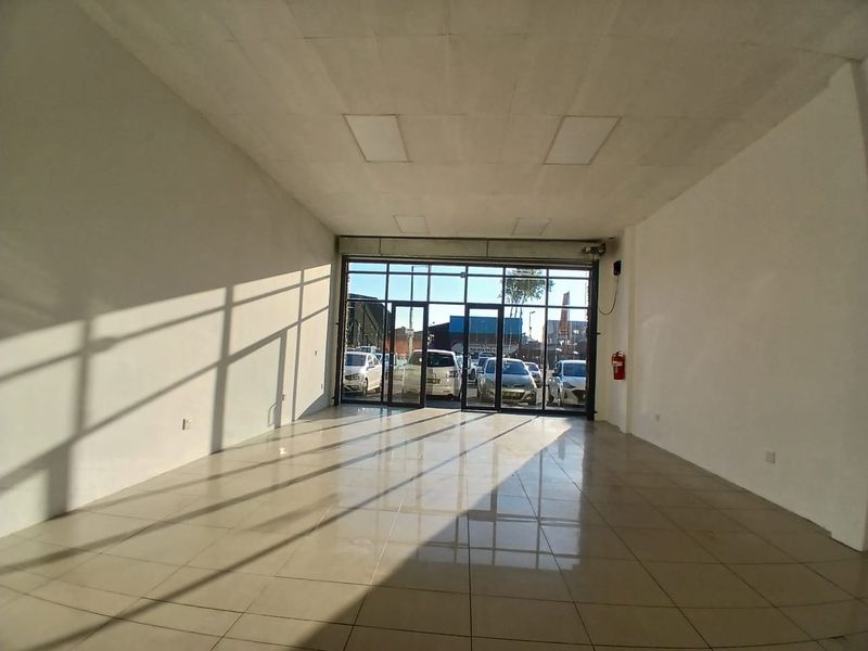 A bright, open-plan retail space featuring tiled flooring, a suspended ceiling, and a large glass storefront providing excellent visibility.