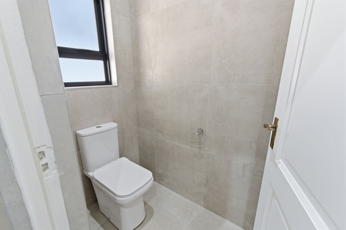 A compact, modern guest bathroom featuring neutral large-format wall and floor tiles, a contemporary toilet, and a window for natural light.