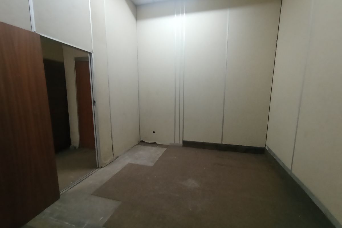 An empty industrial office space featuring modular wall paneling, worn carpeting, and a doorway leading to an adjacent room.
