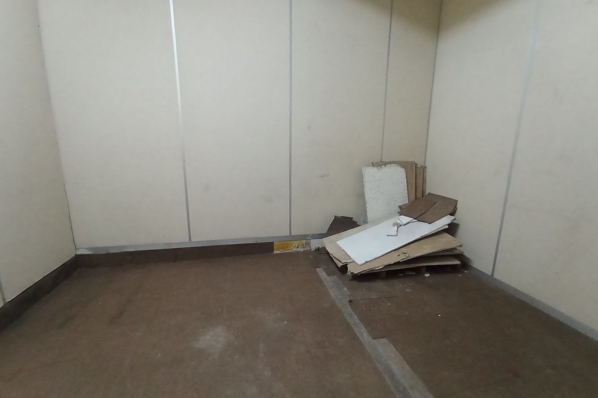 An empty industrial utility space featuring modular wall paneling and worn flooring, suitable for storage or workshop conversion.