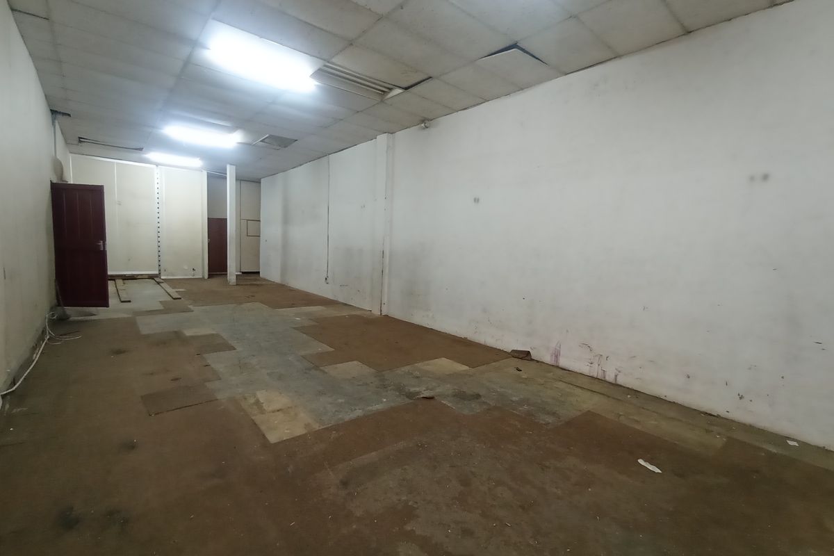 An empty industrial warehouse or commercial space featuring a suspended ceiling, concrete flooring, and basic lighting, suitable for renovation or storage use.