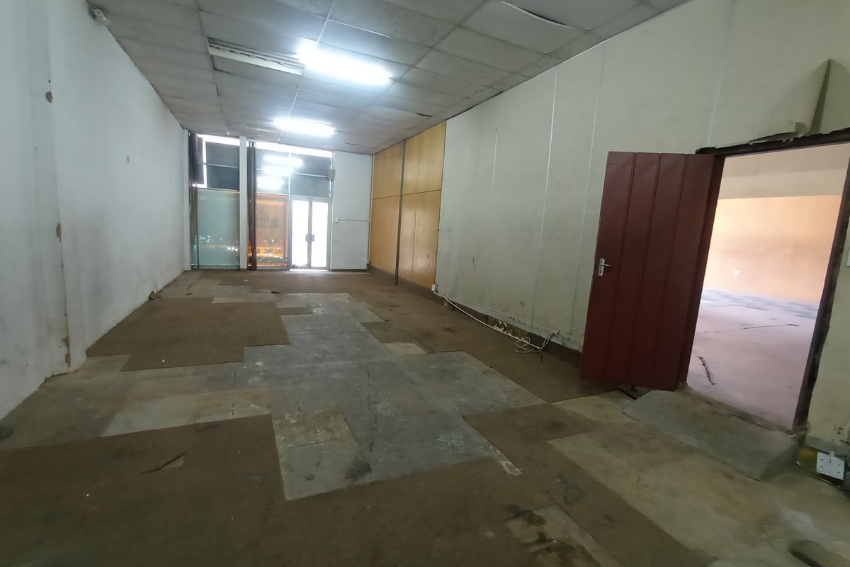An empty industrial or commercial space featuring a drop ceiling, concrete flooring with remnants of carpet, and direct access to an adjacent room.
