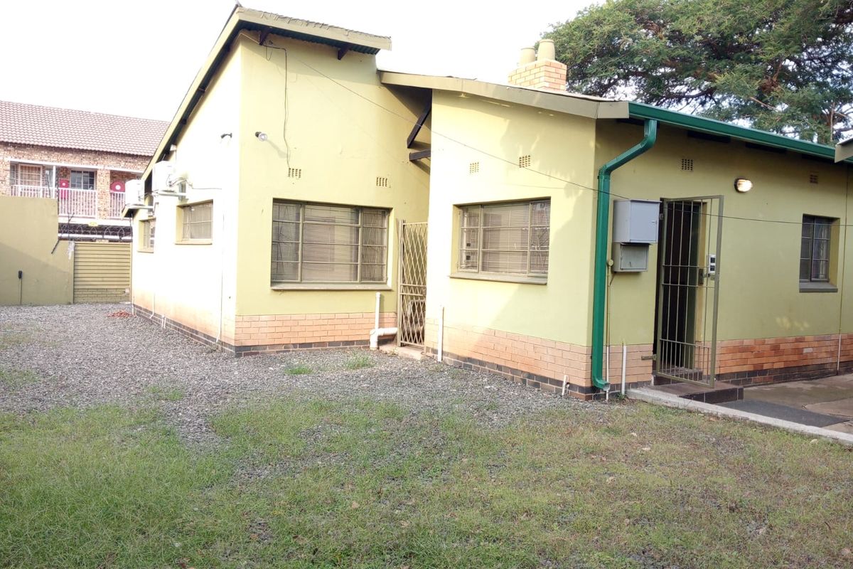 Rear exterior view of the office building featuring brick and painted wall finishes, metal security gates, and functional guttering.