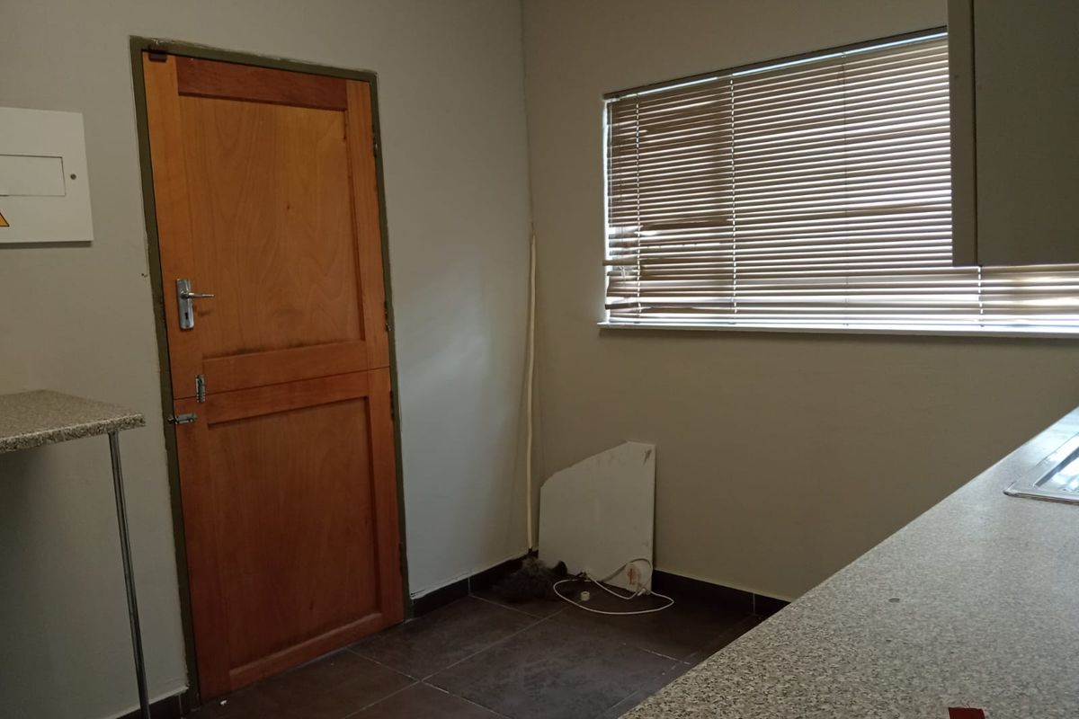 A functional kitchen area featuring tiled flooring, a timber door, and laminate countertops, currently vacant and awaiting updates.