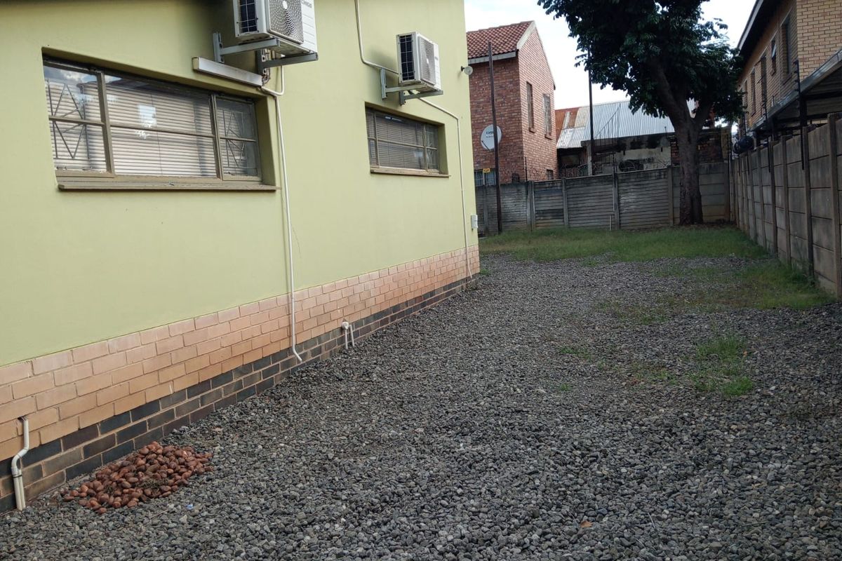 Rear exterior view of the office building featuring a gravel yard, brick base detailing, and wall-mounted air conditioning units.