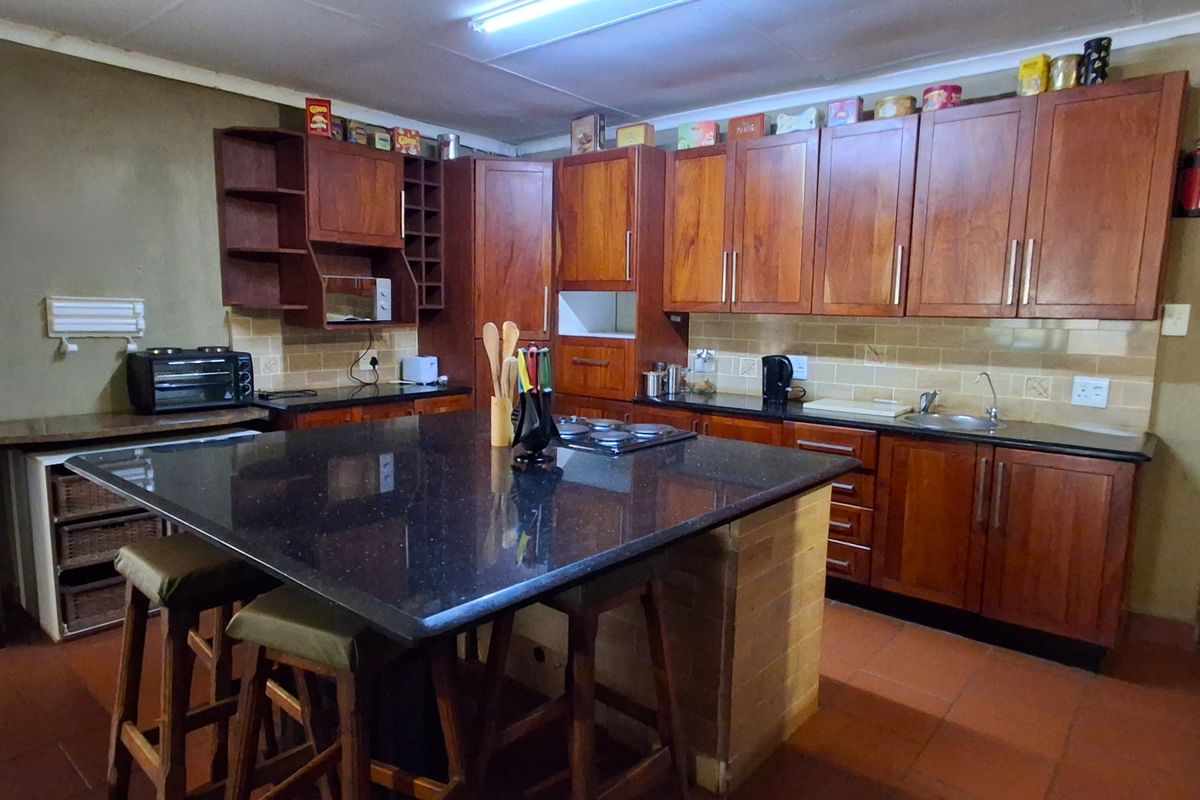 A functional kitchen featuring wooden cabinetry, granite countertops, a central island with a built-in hob, and tiled backsplash, offering ample storage and workspace.