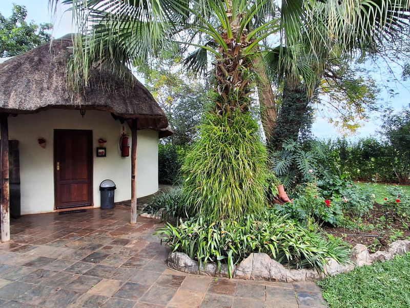 A charming lodge unit featuring a traditional thatch roof, stone-tiled patio, and direct access to a well-maintained garden area.