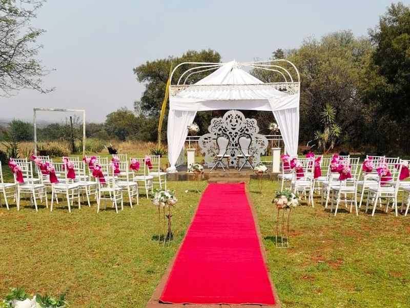Outdoor garden event space featuring a raised stone platform with a decorative metal gazebo frame, set within a landscaped lawn area.