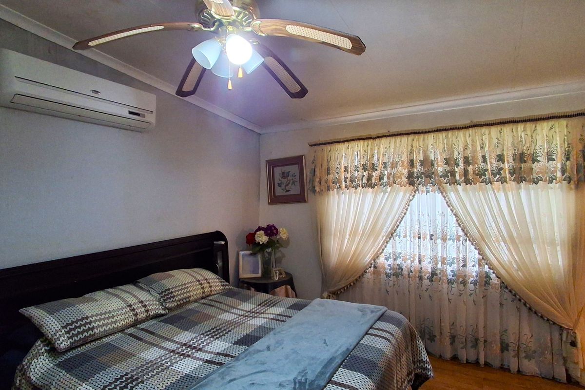 A bedroom featuring a ceiling fan, split-system air conditioning unit, and timber flooring, providing a functional and comfortable sleeping space.