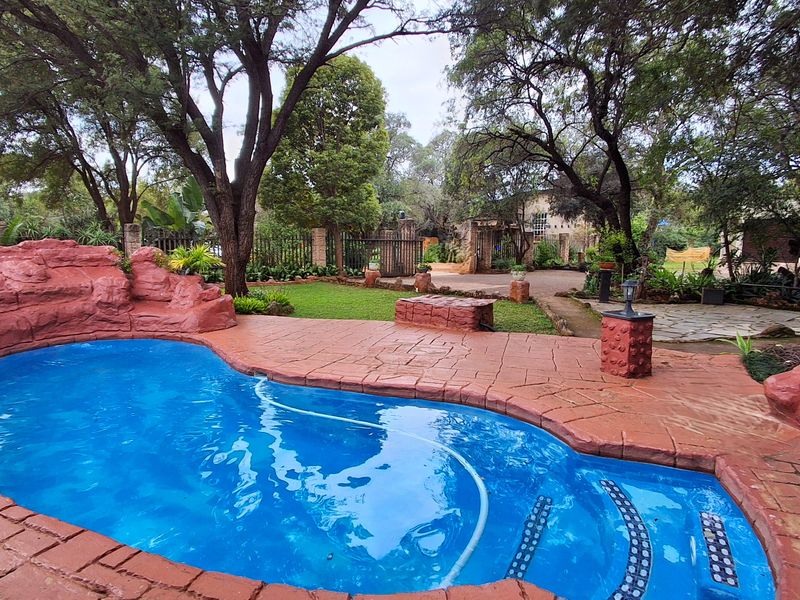 A well-maintained outdoor pool area featuring a custom rock-feature surround, paved decking, and established garden landscaping within a secure property setting.