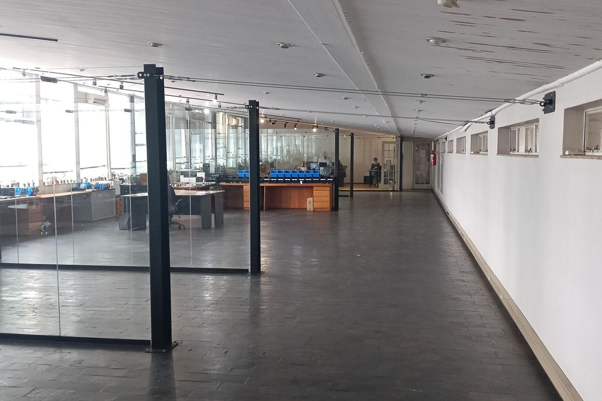 Spacious open-plan office area featuring glass partitions, dark tiled flooring, and an exposed ceiling with recessed lighting.