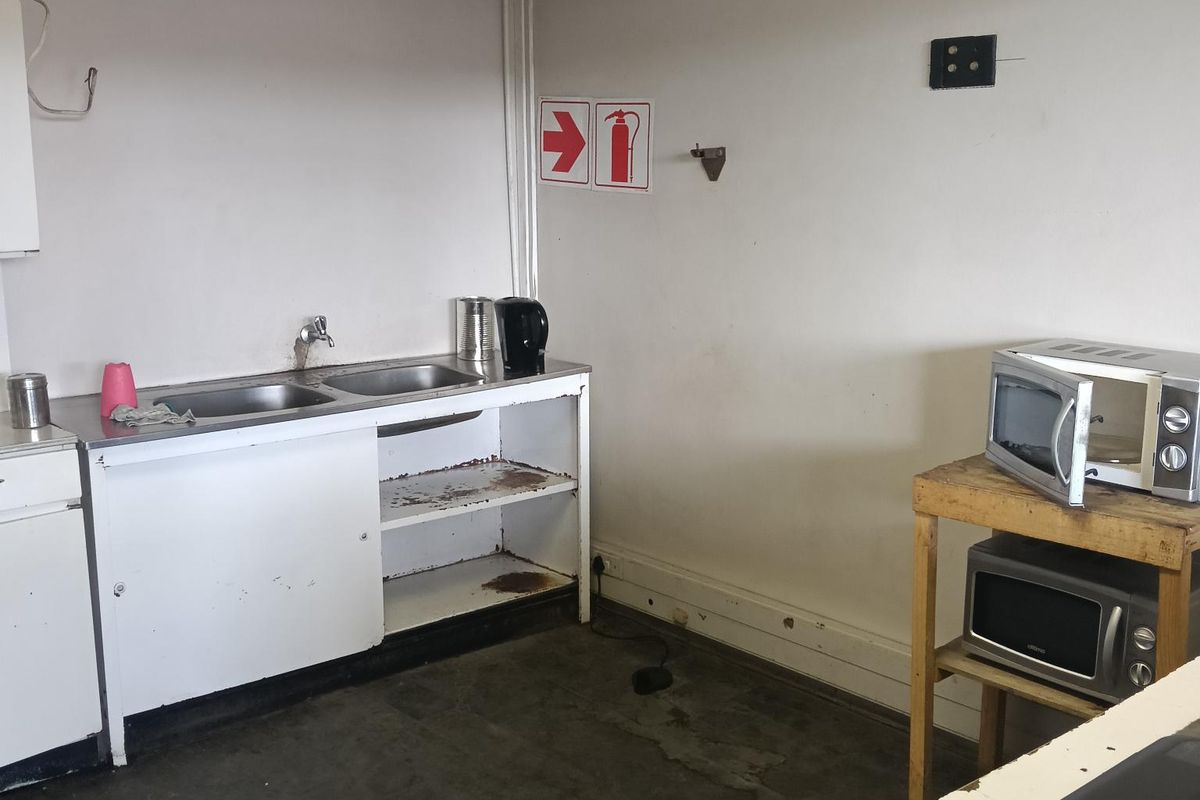 A basic industrial kitchenette featuring a stainless steel sink, open shelving, and drop ceiling, currently in need of maintenance and refurbishment.