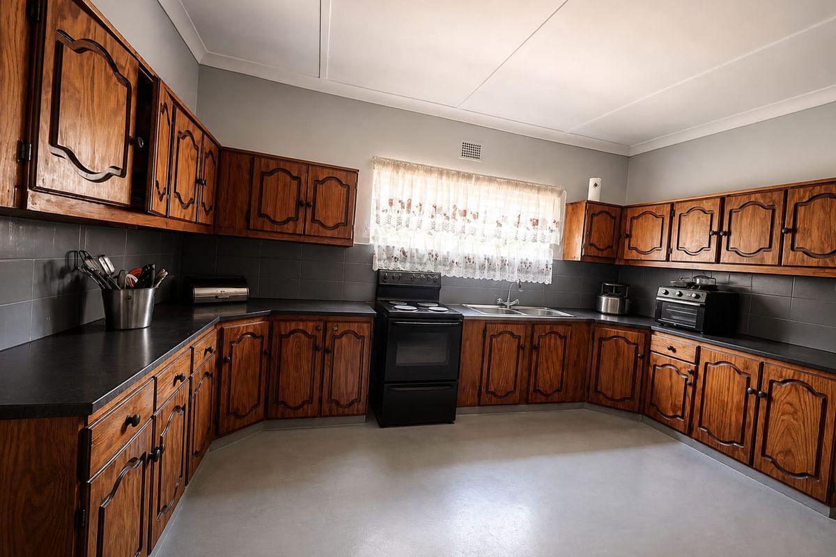 A functional kitchen featuring traditional wooden cabinetry, dark laminate countertops, a freestanding stove, and a double basin sink with a tiled backsplash.