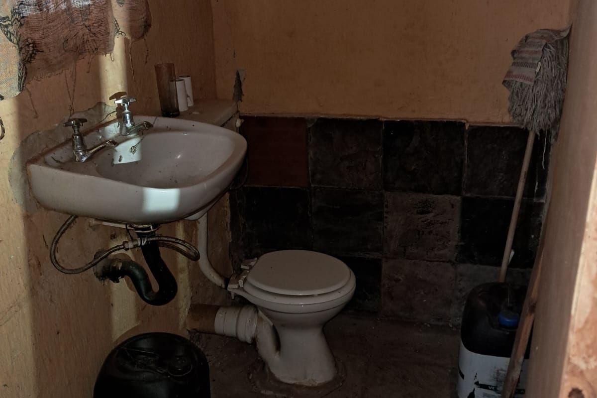 A small, dated bathroom featuring a wall-mounted basin and a standard toilet, requiring significant renovation and cosmetic updates to improve functionality and appearance.