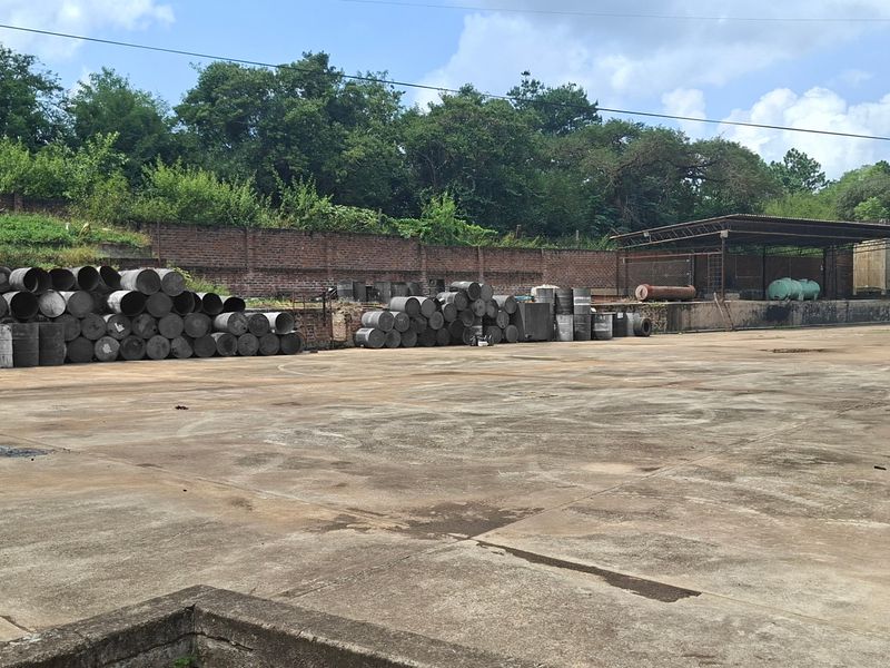 Large industrial concrete yard featuring a covered loading bay, brick boundary wall, and extensive open storage space for operational use.