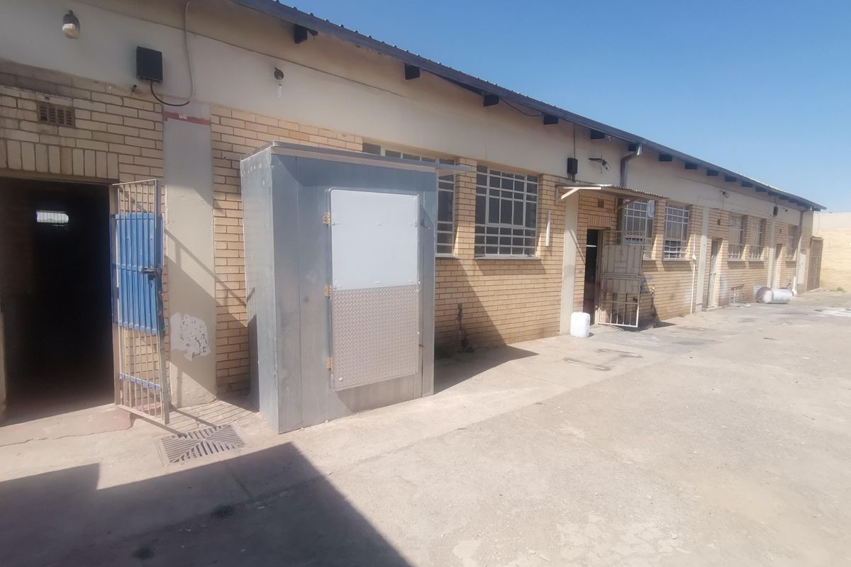 Exterior view of a commercial building featuring brick facade, metal security gates, and a standalone metal utility enclosure on a concrete yard.