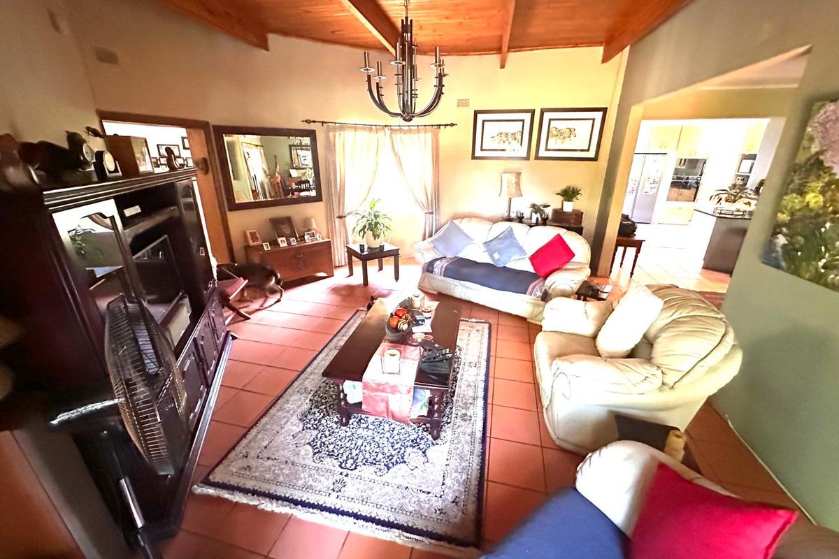 Spacious living room featuring high exposed timber beam ceilings, terracotta floor tiles, and a central wrought iron chandelier, with an open flow to the kitchen.