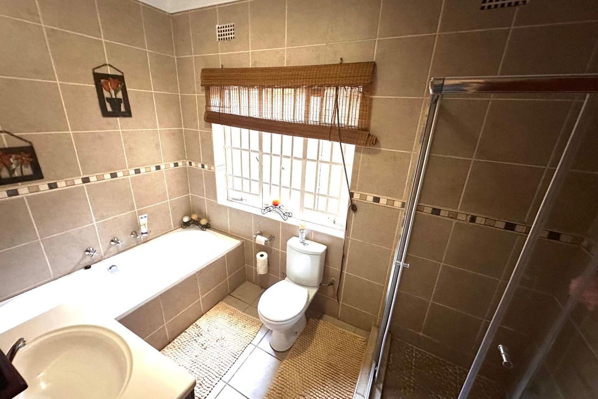 A functional bathroom featuring a built-in bathtub, separate shower enclosure, vanity basin, and toilet with neutral wall and floor tiling.
