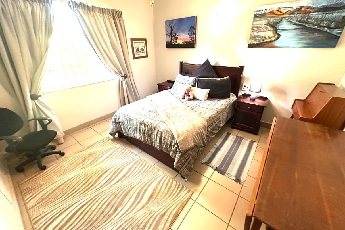 A functional bedroom featuring tiled flooring and a window fitted with security bars, providing natural light and a secure environment.