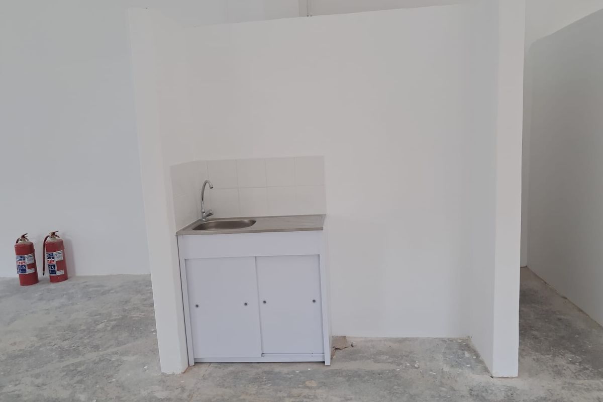 A functional kitchenette area featuring a stainless steel sink, built-in white cabinetry, and tiled splashback, situated within an open industrial space.