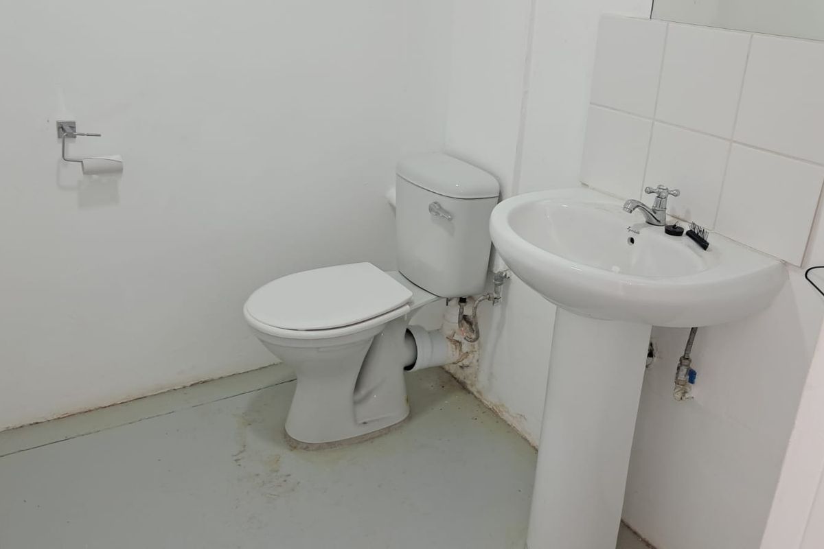 A functional industrial-style restroom featuring a pedestal basin, standard toilet, and tiled splashback.