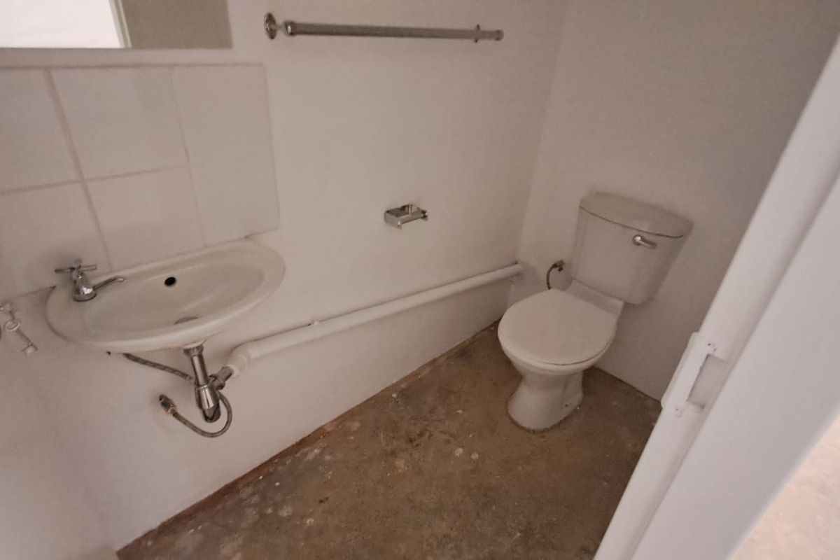 A compact industrial-style bathroom featuring a basic wall-mounted basin, toilet, and exposed plumbing, currently requiring flooring and wall finishing.