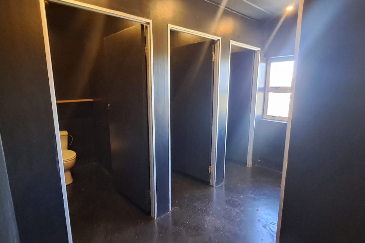 A functional industrial-style restroom facility featuring multiple individual toilet cubicles with dark painted walls and durable flooring.
