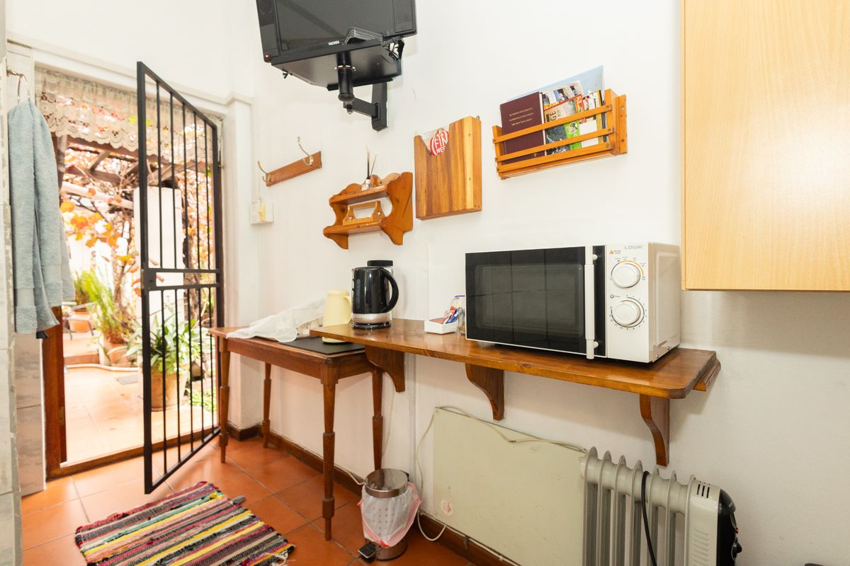 A compact kitchenette area featuring a wooden prep counter, wall-mounted shelving, and direct access to an outdoor patio through a security gate.