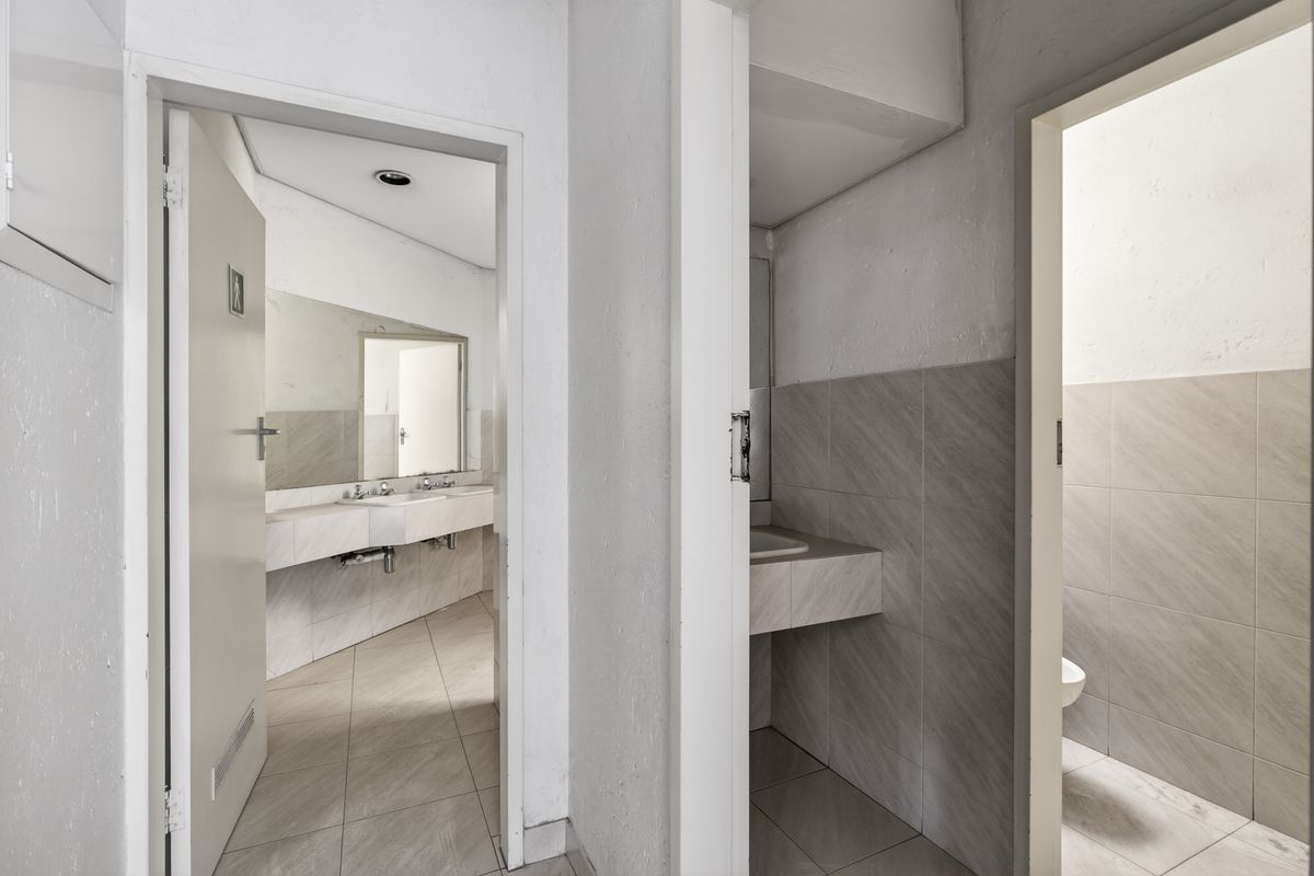 A functional office restroom facility featuring tiled walls, built-in vanity basins, and separate toilet cubicles with neutral finishes.