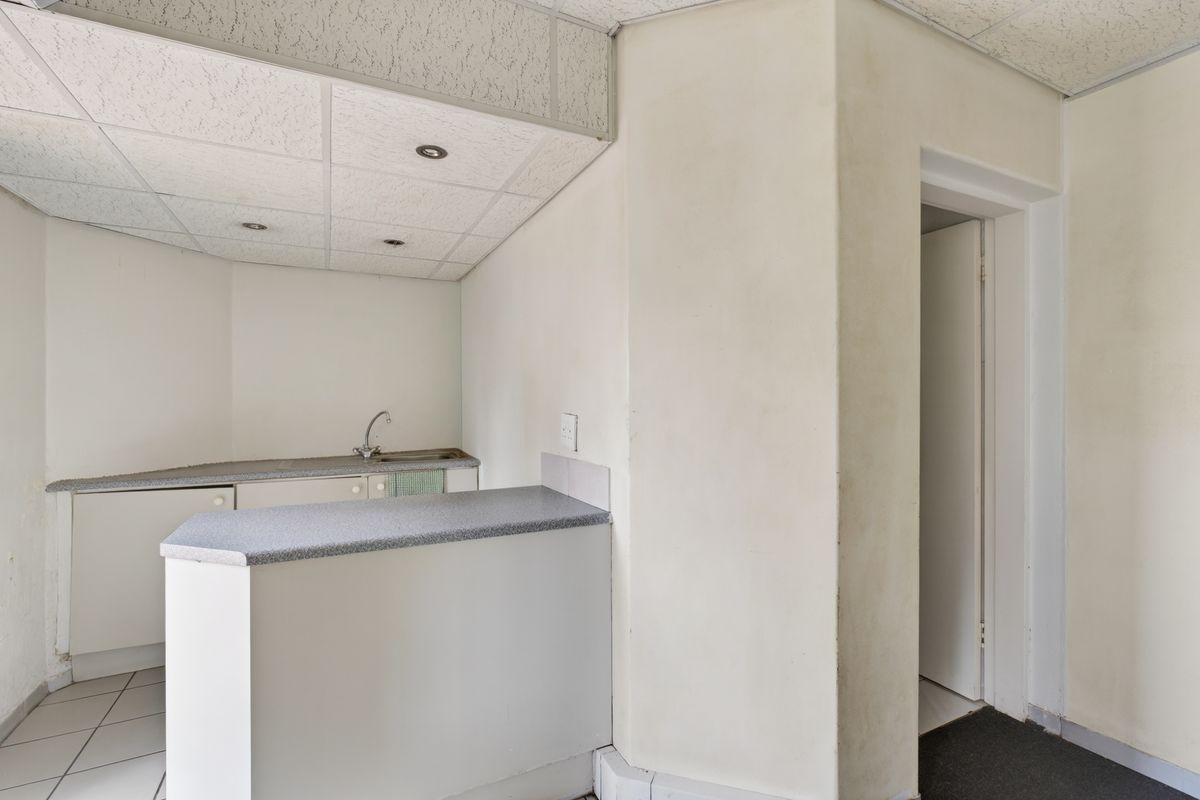 A compact office kitchenette featuring a small counter, sink, and drop ceiling, providing basic utility space for a professional environment.