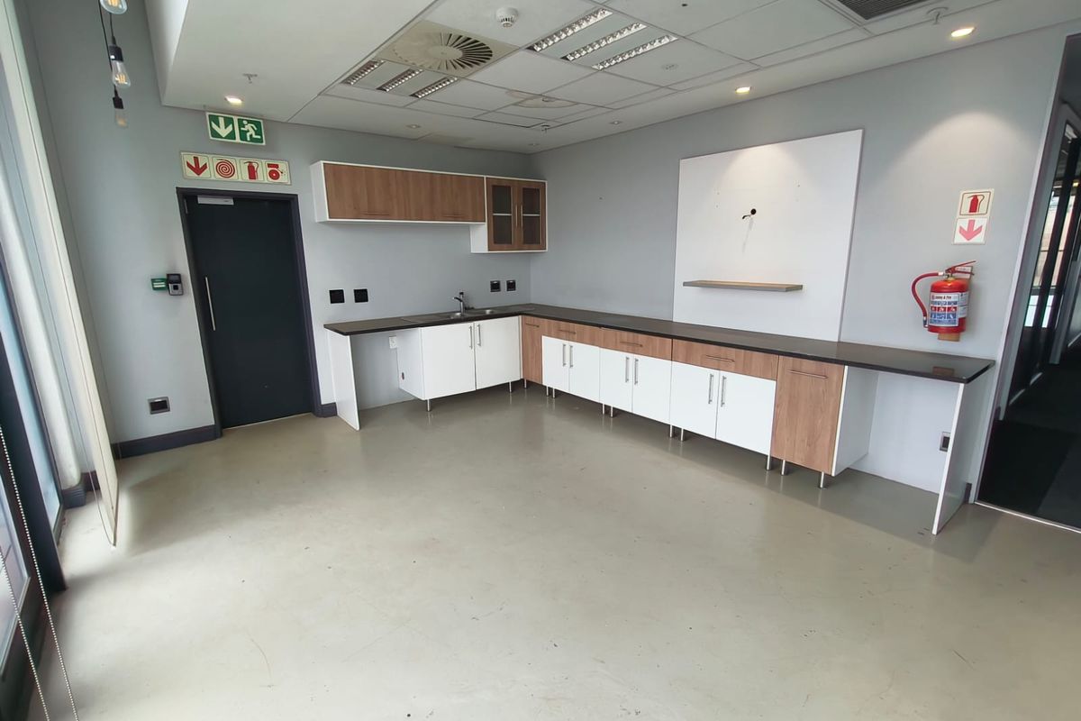 A functional office kitchenette featuring built-in cabinetry, a sink, and integrated workspace, finished with modern surfaces and a suspended ceiling.