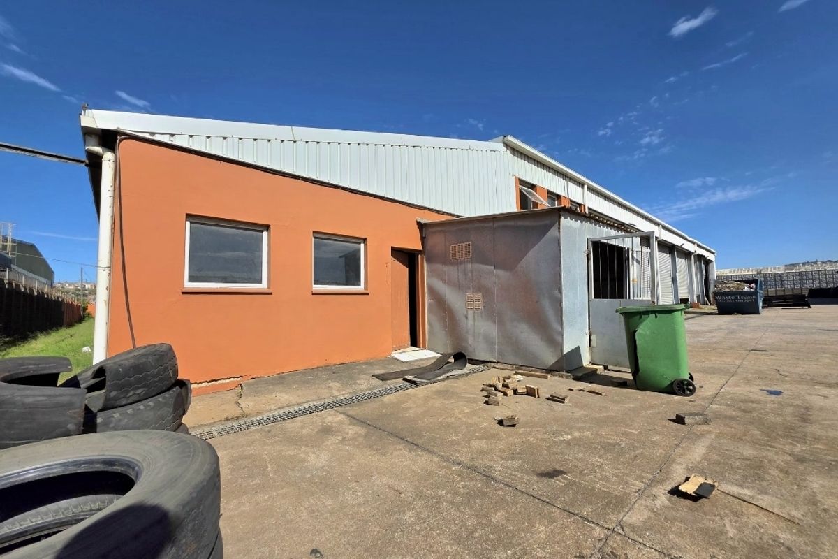Rear exterior view of an industrial warehouse facility featuring metal cladding, concrete apron, and multiple roller door access points.