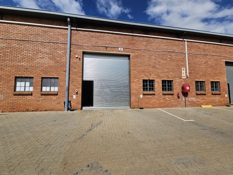 Industrial warehouse unit featuring a red brick facade, roller shutter door, and paved exterior parking area.