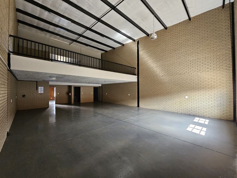 Spacious industrial warehouse unit featuring high ceilings, exposed brick walls, polished concrete flooring, and a mezzanine level with a safety railing.