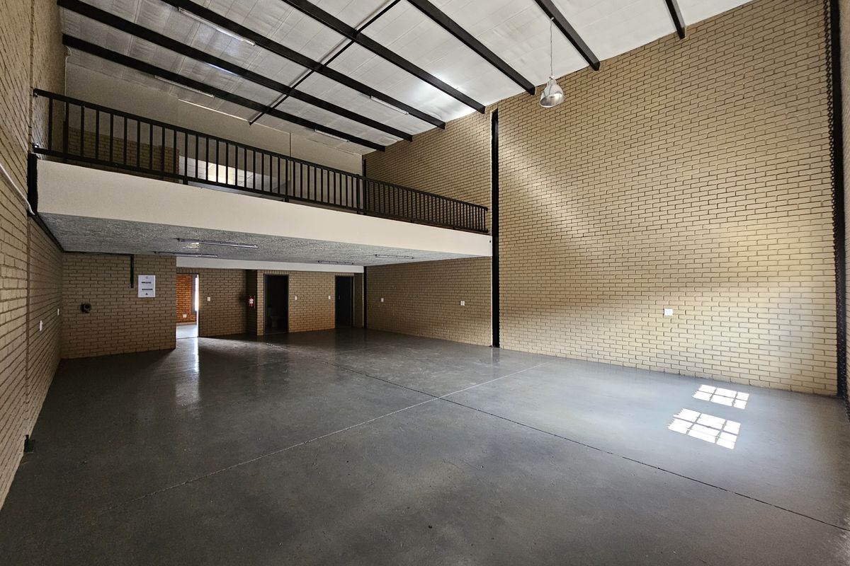 Spacious industrial warehouse unit featuring high ceilings, exposed brick walls, polished concrete flooring, and a mezzanine level with a safety railing.