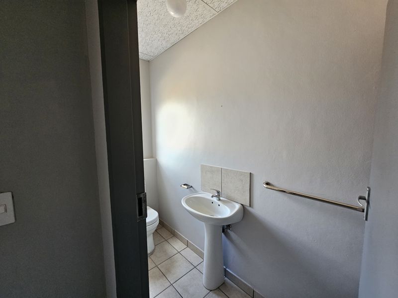 A functional industrial restroom featuring a pedestal basin, tiled flooring, and a wall-mounted grab rail.