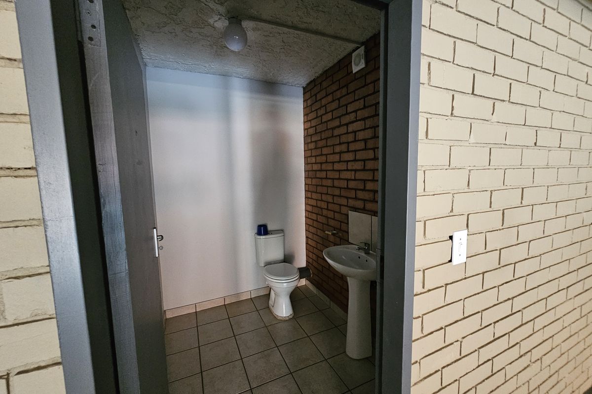 A functional industrial-style restroom featuring a pedestal basin, toilet, tiled flooring, and exposed brick wall finishes.