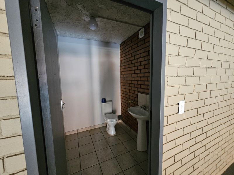 A functional industrial-style restroom featuring a pedestal basin, toilet, tiled flooring, and exposed brick wall finishes.