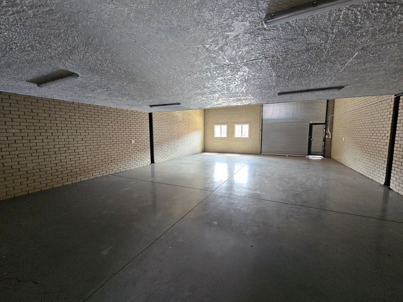 Spacious industrial warehouse unit featuring exposed brick walls, polished concrete flooring, high ceilings with fluorescent lighting, and a large roller shutter door.