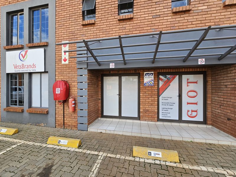 Industrial unit entrance featuring a brick facade, covered entryway with tiled flooring, and glass-paneled double doors with signage.