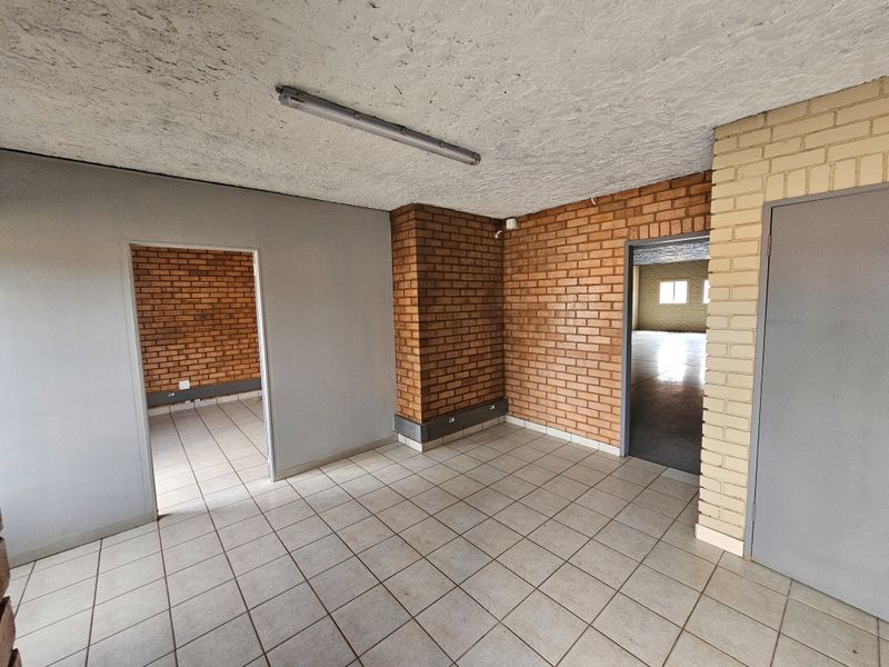 An empty industrial office space featuring exposed brick walls, tiled flooring, and fluorescent lighting, providing a versatile layout for business operations.