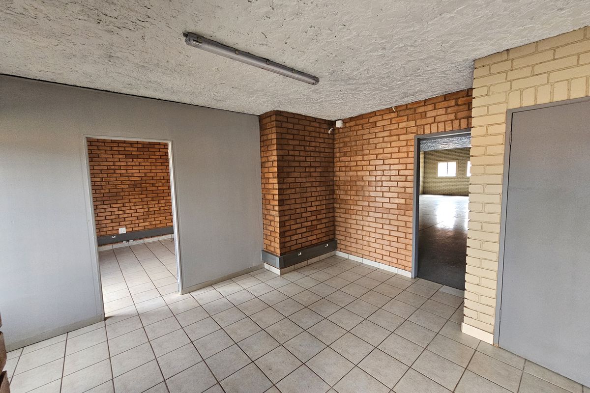 An empty industrial office space featuring exposed brick walls, tiled flooring, and fluorescent lighting, providing a versatile layout for business operations.